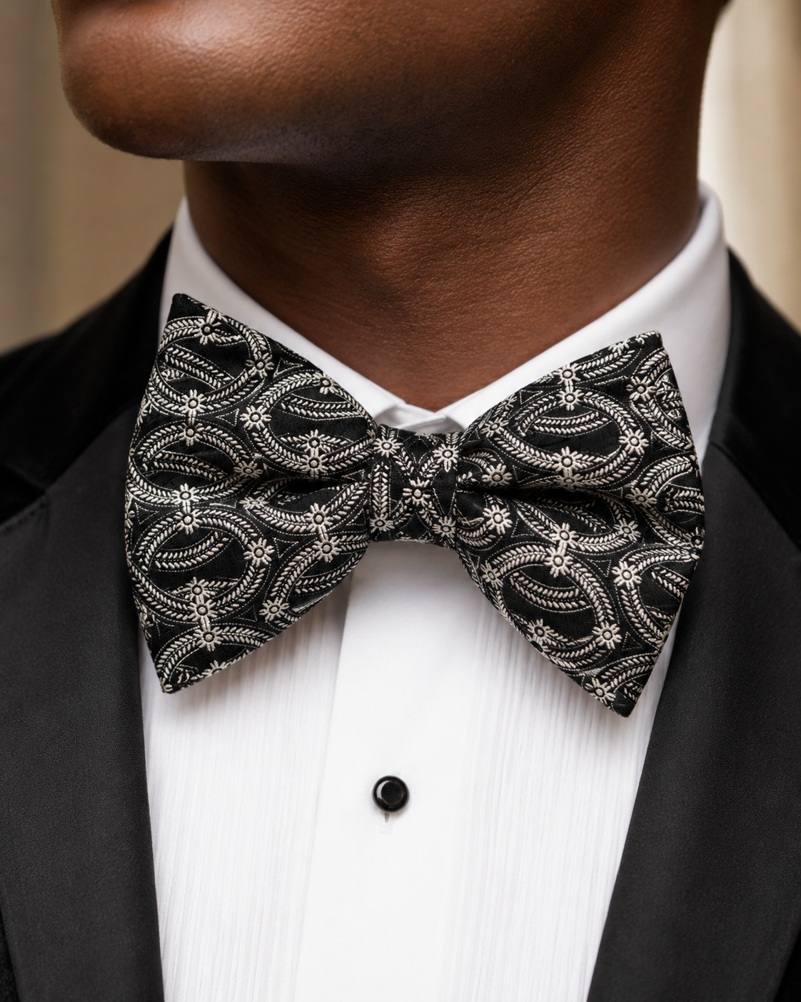 Close-up portrait of a man wearing a black and silver patterned bow tie with a white tuxedo shirt and black dinner jacket.
