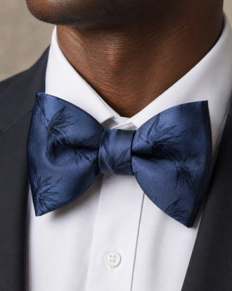 Close-up portrait of a man wearing a midnight blue satin floral bow tie with a white shirt and black tuxedo.