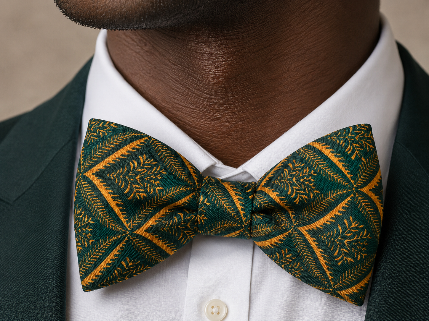 Close-up portrait of a man wearing an emerald green and gold patterned bow tie with a white shirt and dark suit.
