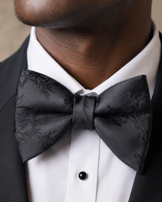 Close-up portrait of a man wearing a black satin floral bow tie with a white shirt and black tuxedo.