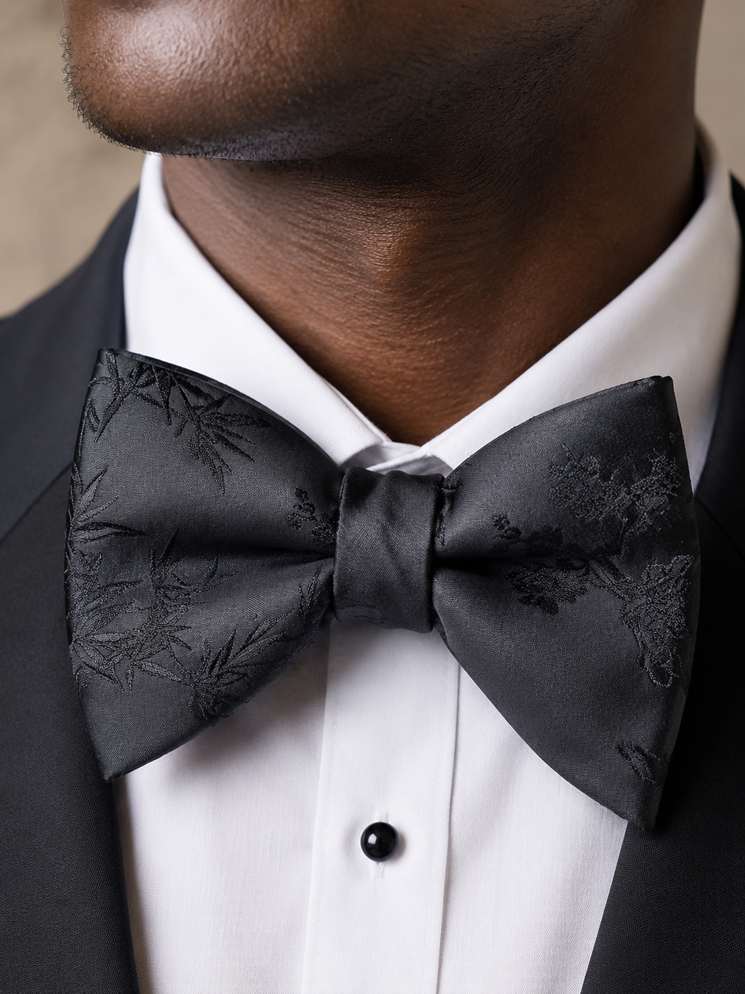 Close-up portrait of a man wearing a black satin floral bow tie with a white shirt and black tuxedo.