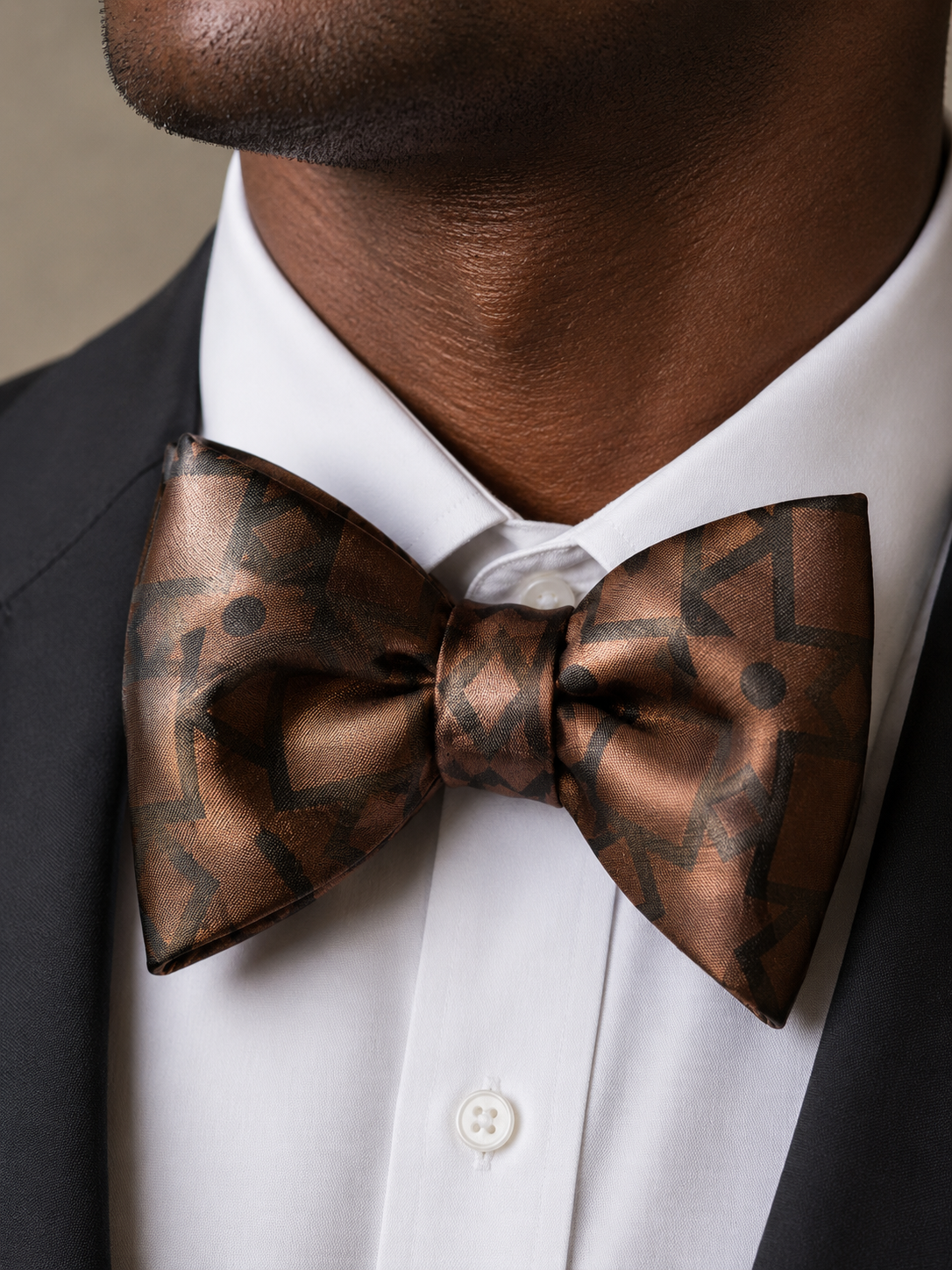 Close-up portrait of a man wearing a bronze geometric bow tie with a white shirt and black tuxedo.